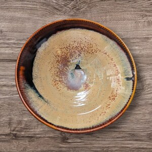 Peut inclure: Un bol en céramique fait à la main avec un glaçage unique. Le bol présente un bord marron qui se transforme en un centre beige avec des accents bruns et bleus mouchetés. Le bol est rond et a une finition brillante.