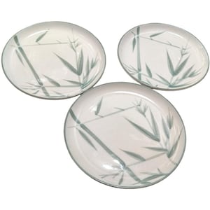 May include: A set of three round ceramic plates featuring a white base color and a painted green bamboo stalk and leaf pattern. Each plate has a smooth surface and a thin green rim, displaying a consistent botanical design across all three pieces.