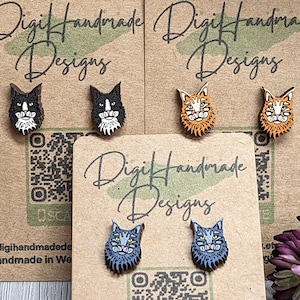 May include: A set of six wooden cat earrings. The earrings are in the shape of cat faces with different colored fur. The earrings are displayed on a brown card with the text "Digi Handmade Designs" and a QR code.