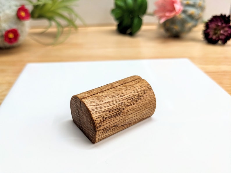May include: A small, wooden, brown, cylindrical table number holder with a slot for a card. The holder is made of natural wood with a rustic finish.
