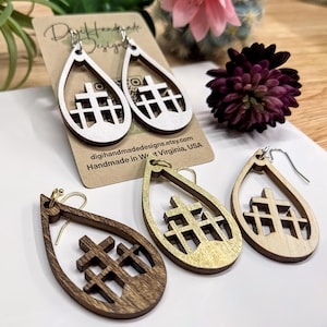 May include: Three pairs of wooden teardrop-shaped earrings with a cross design. The earrings are in natural wood, gold, and dark brown.