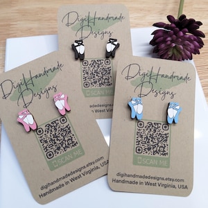 May include: Three cards with the text "Digi Handmade Designs" and a QR code. Each card features a pair of wooden earrings shaped like ballet shoes. The earrings are in pink, black, and blue.