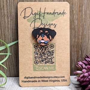 May include: A wooden cutout of a Rottweiler dog head with black and brown fur, a pink tongue, and blue eyes. The cutout is on a brown card with the text "Digi Handmade Designs" and a QR code with the text "Scan Me". The card also includes the text "digihandmadedesigns.etsy.com" and "Handmade in West Virginia, USA".