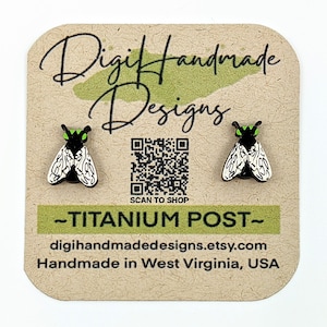 May include: A pair of black and white fly earrings with green accents. The earrings are on a card with the text "Digi Handmade Designs" and a QR code that says "Scan to Shop". The card also says "Titanium Post" and "digihandmadedesigns.etsy.com". The card also says "Handmade in West Virginia, USA".