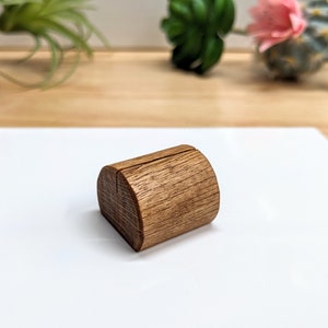 May include: A wooden, half-round, table number holder with a slot for a card. The holder is made of natural wood with a brown finish.