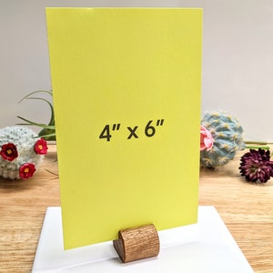 May include: A bright yellow card with the text "4" x "6" printed on it. The card is standing on a wooden easel.