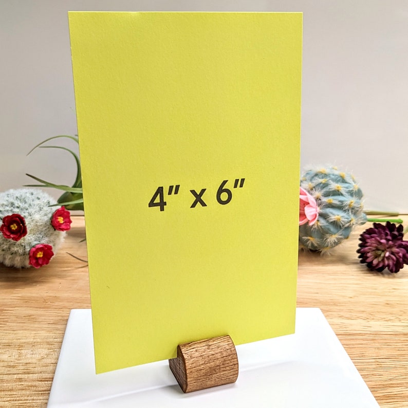 May include: A bright yellow card with the text "4" x "6" printed on it. The card is standing on a wooden easel.
