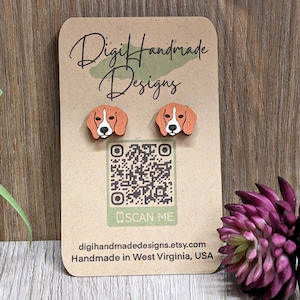 May include: A pair of wooden earrings featuring a beagle dog design. The earrings are brown and white with a natural wood finish. The earrings are displayed on a card with the text "Digi Handmade Designs" and a QR code with the text "SCAN ME".