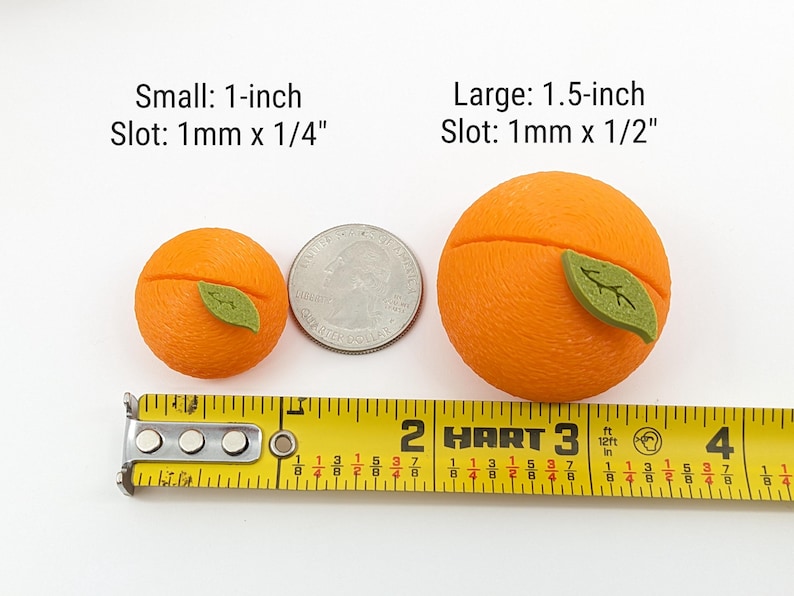 May include: Two orange-colored, spherical objects with green leaf accents, one 1-inch and the other 1.5-inch, are displayed next to a US quarter and a yellow measuring tape. Text indicates slot sizes.