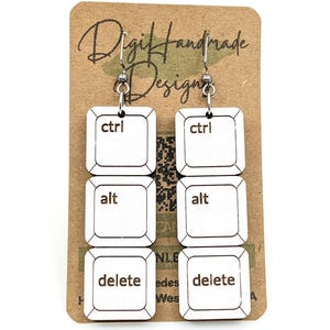 May include: White keyboard key earrings with the words "ctrl", "alt", and "delete" printed on them. The earrings are hanging from silver hooks. The earrings are on a brown card with the words "Digi Handmade Designs" printed on it.