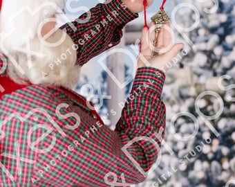 May include: A decorative antique key with a red string, held against a festive background. The key is gold-colored with intricate detailing. The person is wearing a red and green plaid shirt and a Santa hat.