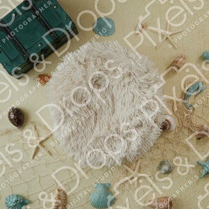 May include: A white faux fur round pouf sits on a beige background with a blue and green fishing net, seashells, and starfish scattered around it. A teal green wooden treasure chest is in the upper left corner of the image.