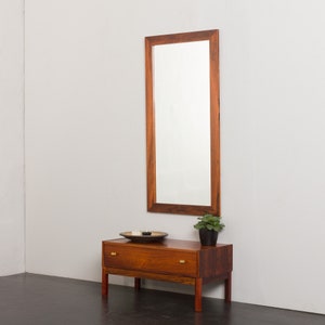 Puede incluir: Un tocador de madera con un solo cajón y un gran espejo rectangular encima. El tocador está hecho de madera oscura con un tono rojizo y tiene herrajes de latón. El espejo está enmarcado en la misma madera que el tocador.