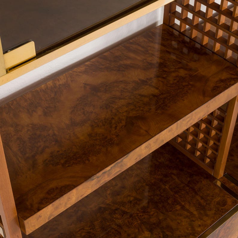 K&ouml;nnte beinhalten: Ein Holzregal mit einem Gittermuster an den Seiten und einer braunen Holzfurnierplatte. Das Regal hat eine goldene Metallverkleidung.