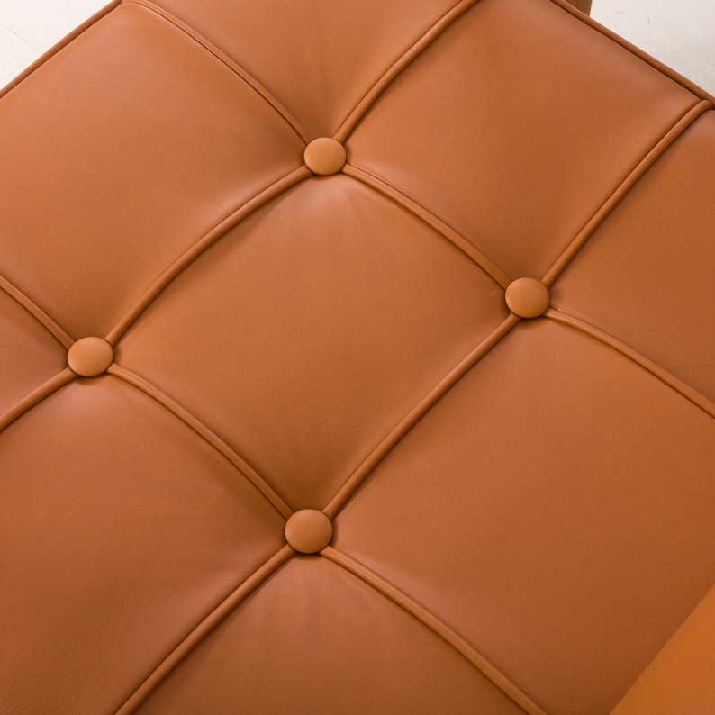 May include: Close-up of a brown leather chair with button tufting. The chair has a diamond pattern with four buttons in each diamond.