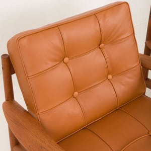 May include: A brown leather armchair with a tufted back and wooden arms. The chair has a simple, mid-century modern design.