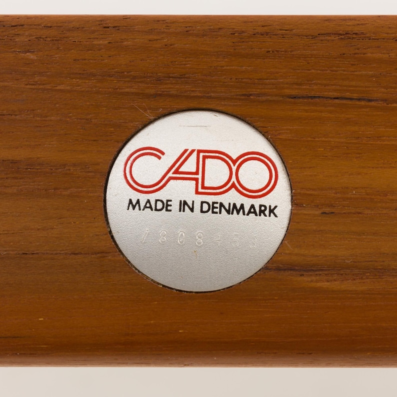 May include: A silver circular label with the text "CADO MADE IN DENMARK" in red lettering. The label has a number "7808" printed below the text.