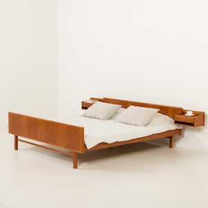 Può includere: Una struttura letto in legno con una calda finitura marrone, dotata di una testiera che si estende in due comodini sospesi integrati. Il letto è coperto da un lenzuolo bianco e due cuscini bianchi abbinati, creando un aspetto pulito e uniforme.