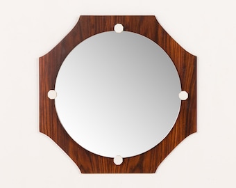 May include: A round mirror with a dark wood octagonal frame. The frame has a rich, dark brown wood grain pattern. Four small, white, circular accents are evenly spaced around the mirror's edge. The mirror reflects the surrounding environment.