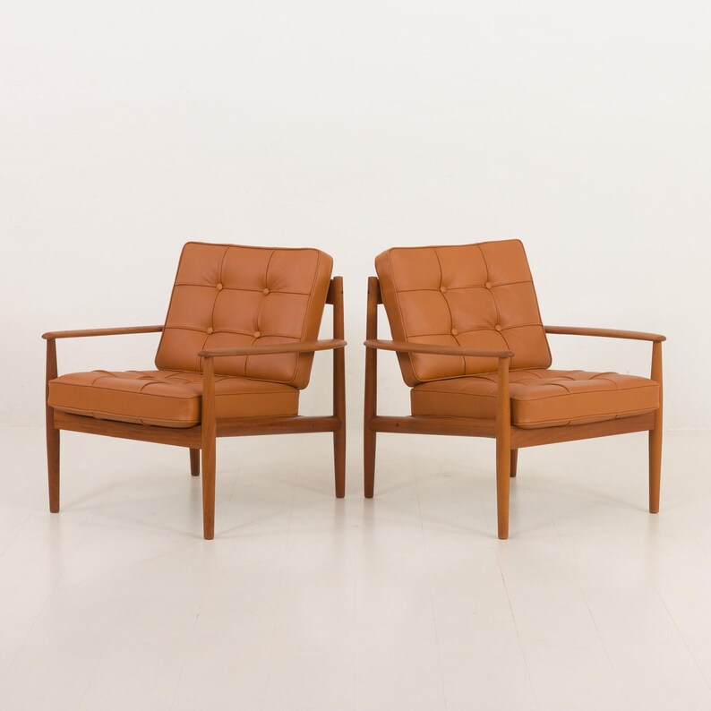 May include: Two brown leather armchairs with wooden frames. The chairs have a tufted design and are positioned side by side on a white background.