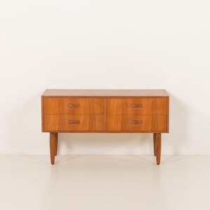 May include: A mid-century modern wooden dresser with four drawers. The dresser is made of light brown wood and has a rectangular shape. The drawers have unique, bow-tie shaped handles. The dresser stands on four tapered legs.