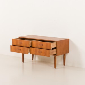 May include: A mid-century modern wooden dresser with four drawers, two open. The dresser is a warm brown color with tapered legs and wooden drawer pulls. The drawers are open, revealing the interior.