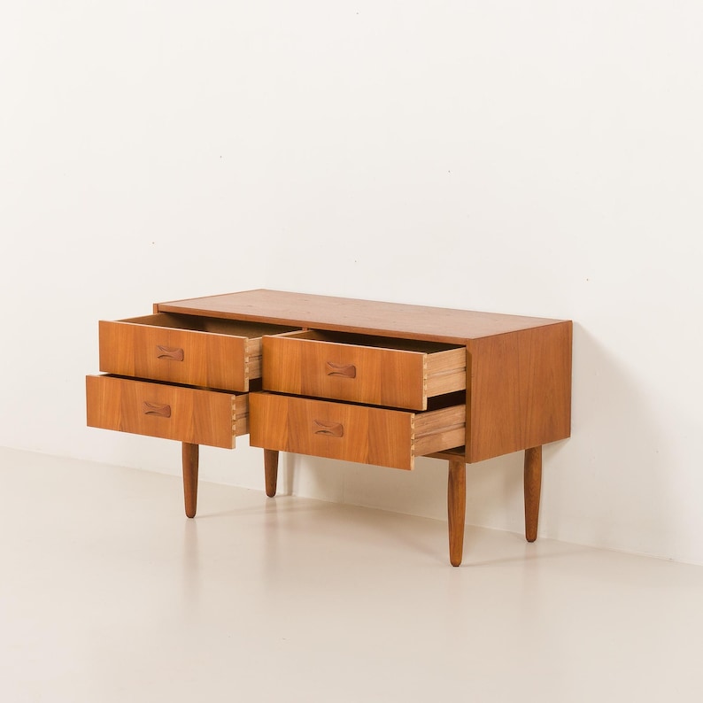 May include: A mid-century modern wooden dresser with four drawers, two open. The dresser is a warm brown color with tapered legs and wooden drawer pulls. The drawers are open, revealing the interior.