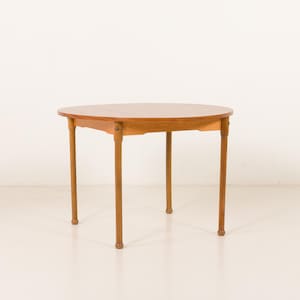 May include: A round, light brown wooden table with four slender, cylindrical legs. The tabletop is a lighter shade of brown than the legs. The table is set against a plain white background. The table is approximately 30 inches in diameter.