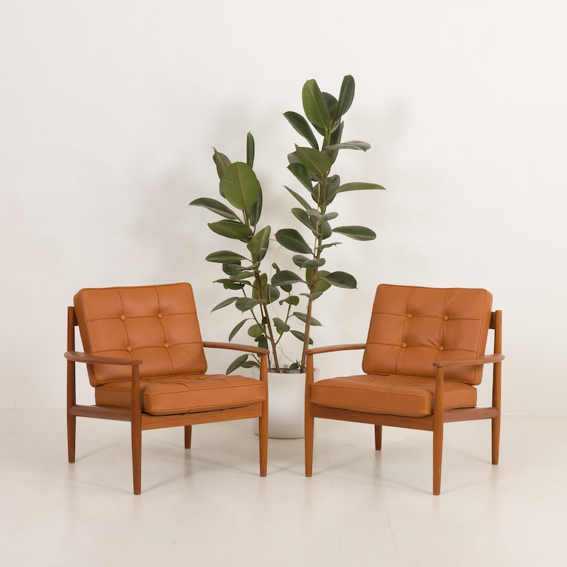 May include: Two brown leather armchairs with wooden frames, positioned in front of a potted plant with green leaves.