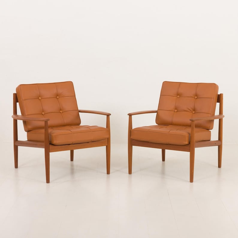 May include: Two brown leather armchairs with tufted upholstery and wooden frames. The chairs are positioned facing each other on a white background.