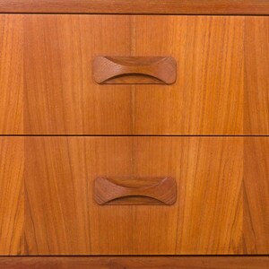 May include: Close-up of a wooden dresser with two drawers. The drawers have a warm, reddish-brown tone with visible wood grain. Each drawer features a unique, curved wooden handle, adding a touch of mid-century modern design.