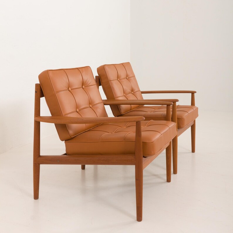 May include: Two brown leather armchairs with wooden frames. The chairs have a tufted design and are arranged side by side.