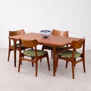Pode incluir: Um conjunto de jantar de meados do século com uma mesa retangular de madeira e quatro cadeiras. As cadeiras têm armações de madeira e almofadas de assento com listras verdes. Uma tigela de vidro azul repousa sobre a mesa, complementando os tons quentes da madeira.