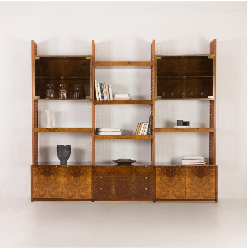 K&ouml;nnte beinhalten: Ein modularer Holz-B&uuml;cherregal mit Glast&uuml;ren und Schubladen. Das B&uuml;cherregal ist aus Holz mit einem Wurzelholzfurnier und hat Messingakzente. Das B&uuml;cherregal hat mehrere Regalbretter und ist ideal zum Aufbewahren von B&uuml;chern, Dekorationsartikeln und anderen Haushaltsgegenst&auml;nden.