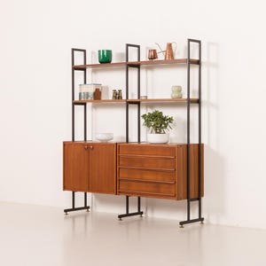 May include: Mid-century modern shelving unit with a wooden cabinet, drawers, and shelves. The unit has a black metal frame and is filled with decorative items and a potted plant. The cabinet doors and drawers are made of wood.