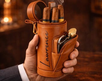 May include: A tan cylindrical leather cigar case featuring the name Lawrence printed in black script. The case holds three cigars and a metal lighter, with an additional exterior pocket containing a metal cigar cutter and a gold-toned lighter.