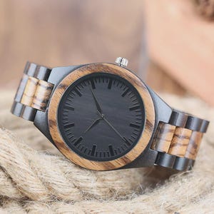 May include: A wristwatch featuring a round face with a black dial and thin hands, encased in a bezel of light brown wood. The link bracelet alternates between dark black wood and light brown wood segments, with a silver crown on the side.