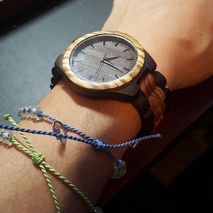May include: A wooden wristwatch with a brown and black striped band. The watch face is black with silver hands and a silver second hand.