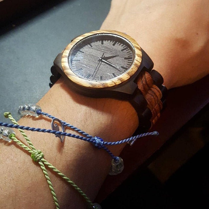 May include: A wooden wristwatch with a brown and black striped band. The watch face is black with silver hands and a silver second hand.