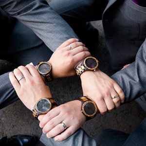 May include: Four men wearing gray suits with brown and black wooden wristwatches. The watches have black faces and brown wooden bands.