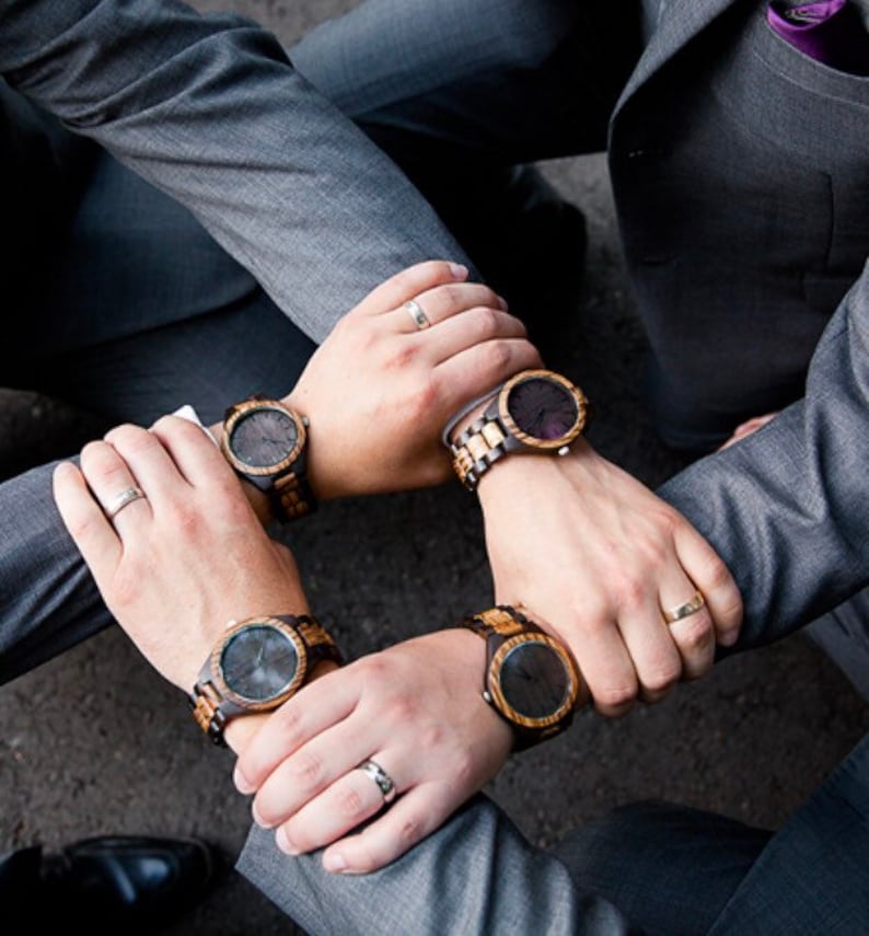May include: Four men wearing gray suits with brown and black wooden wristwatches. The watches have black faces and brown wooden bands.
