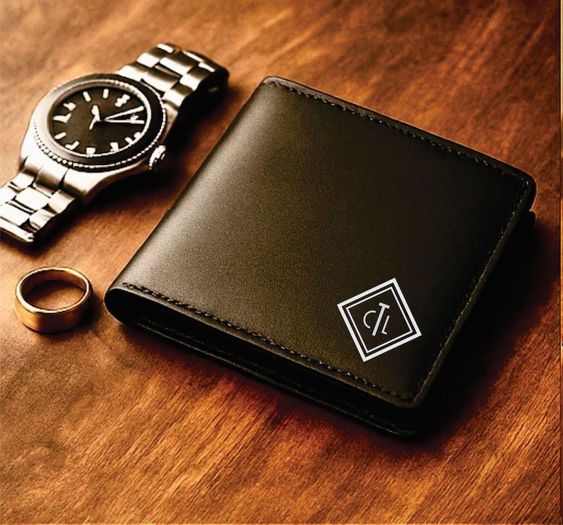 Black leather bifold wallet with a white geometric monogram design featuring the initials “CL” in the bottom corner, displayed on a warm wooden surface beside a silver wristwatch and a gold ring for a classy, masculine presentation.