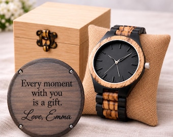 May include: A wooden wristwatch with a black face and a striped wood and black band, displayed on a tan burlap pillow. Beside it is a round wooden plaque engraved with the text: Every moment with you is a gift. Love, Emma. A light wood box is in the back.