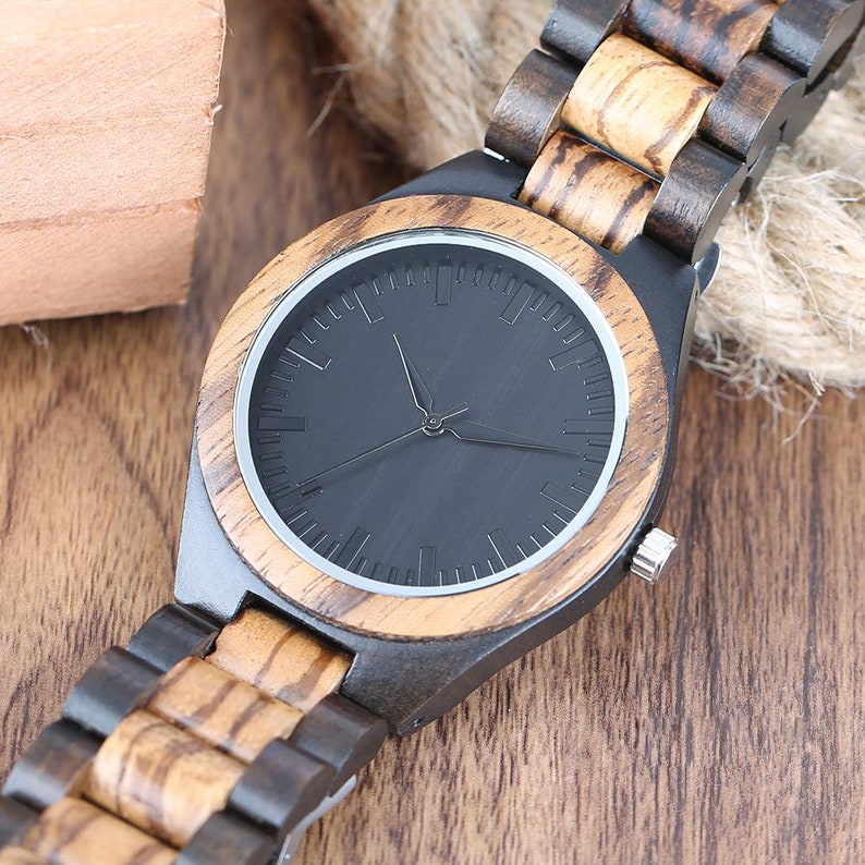 May include: A black and brown wooden wristwatch with a black face and silver hands. The watch has a wooden band with a striped pattern.