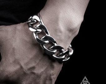 May include: A heavy, polished silver-tone curb chain bracelet featuring thick, interlocking oval links. The bracelet has a high-shine, reflective metallic finish and a substantial, bold design that wraps around the wrist area.