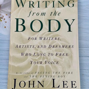 May include: A hardcover book titled "WRITING from the BODY" with dark green lettering on a cream-colored background. The book is by John Lee, with Ceci Miller-Kritsberg. The cover also includes the text "FOR WRITERS, ARTISTS, AND DREAMERS WHO LONG TO FREE YOUR VOICE."
