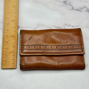May include: A brown leather wallet with a stitched design and a flap closure.