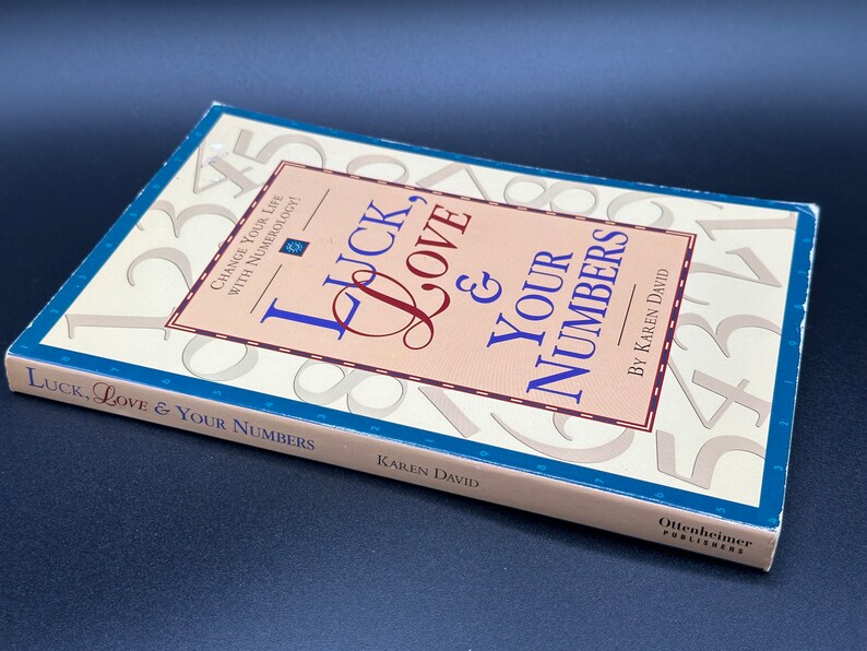 May include: A beige book titled "Luck, Love & Your Numbers" by Karen David. The cover features a background of large numbers and the title is written in a decorative font.
