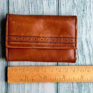 May include: A brown leather wallet with a stitched design and a ruler for scale.