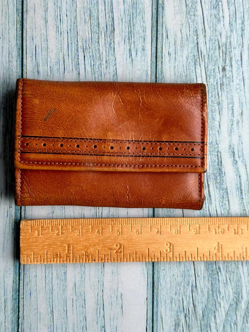 May include: A brown leather wallet with a stitched design and a ruler for scale.